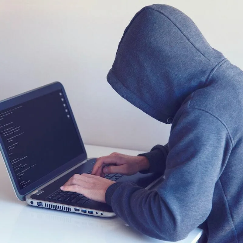 Persona encapuchada frente a una laptop robando datos de tarjetas de crédito
